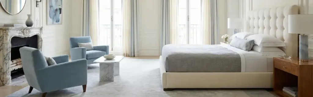 Idées décoration chambre : lit capitonné blanc, fauteuils bleu poudré, cheminée en marbre et rideaux voilés à la parisienne.