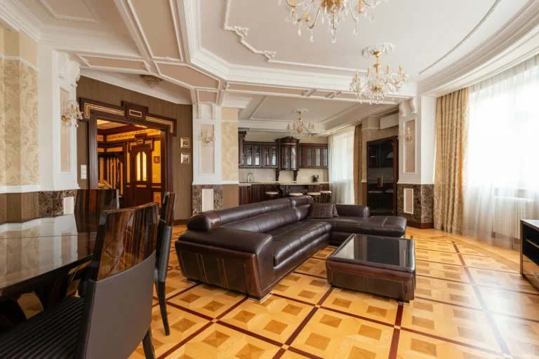 Vaste salon classique avec plafond à caissons stuqués, lustres en cristal, canapé en cuir brun et parquet marqueterie coloré.