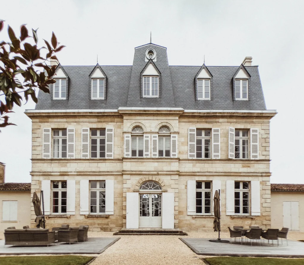 Façade de maison de maître en pierre de taille avec toiture en ardoise, lucarnes, volets blancs et entrée cintrée.